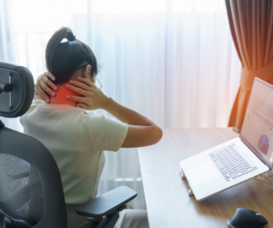 A woman sitting at her workstation and looking at a laptop while holding her neck due to discomfort, highlighting a common reason people seek a chiropractor near Ranceby for neck pain and posture-related issues.